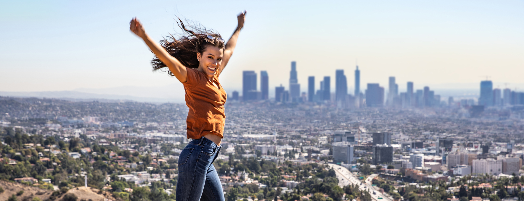 Young tourist/traveller jumping in front of Los Angeles skyline