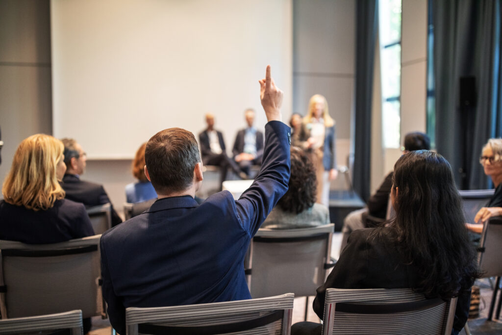Employee inside a conference room raising his hand to ask a question.