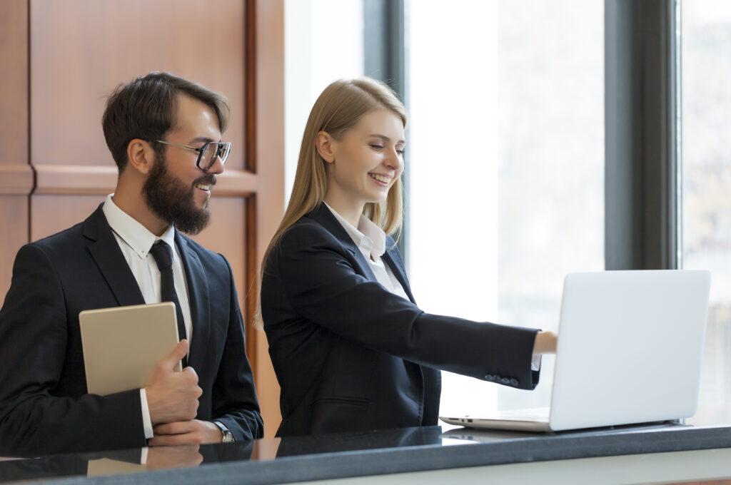 Hotel manager and worker smiling and looking at a laptop screen.