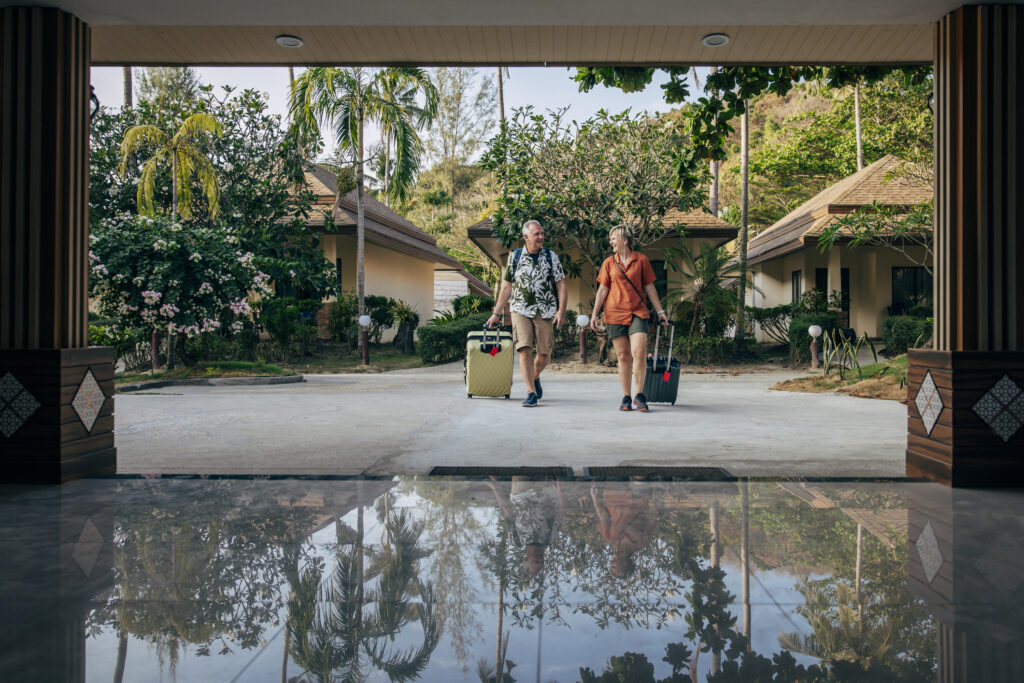 Senior couple smiling and walking into a resort with their luggage
