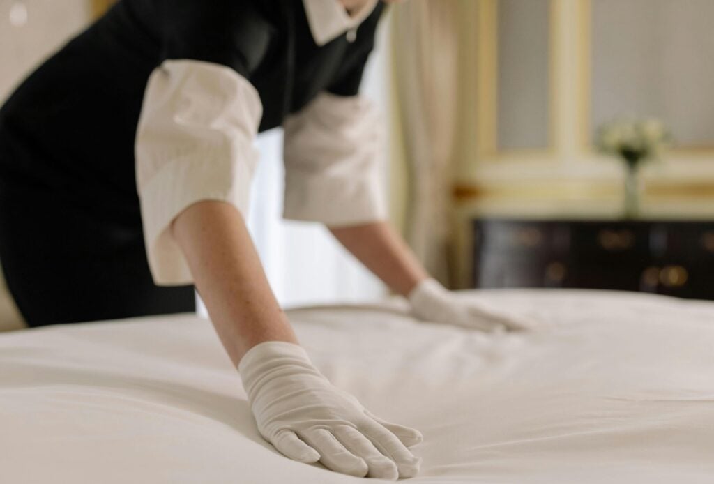 Hotel housekeeper cleaning room and smoothing out the bed
